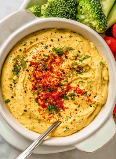 A bowl of creamy deviled egg dip garnished with herbs and served with crackers.