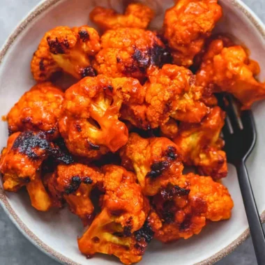 Bowl of easy buffalo cauliflower bites garnished with fresh herbs
