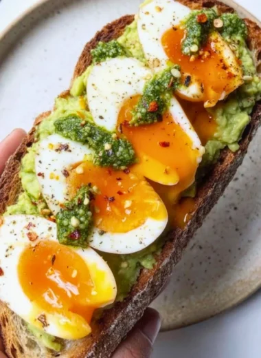 Pesto avocado toast topped with eggs on a plate, showcasing vibrant green colors.