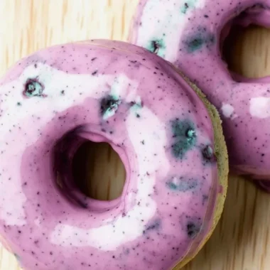 Freshly baked blueberry cake donuts topped with a glaze and blueberries.