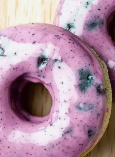 Freshly baked blueberry cake donuts topped with a glaze and blueberries.