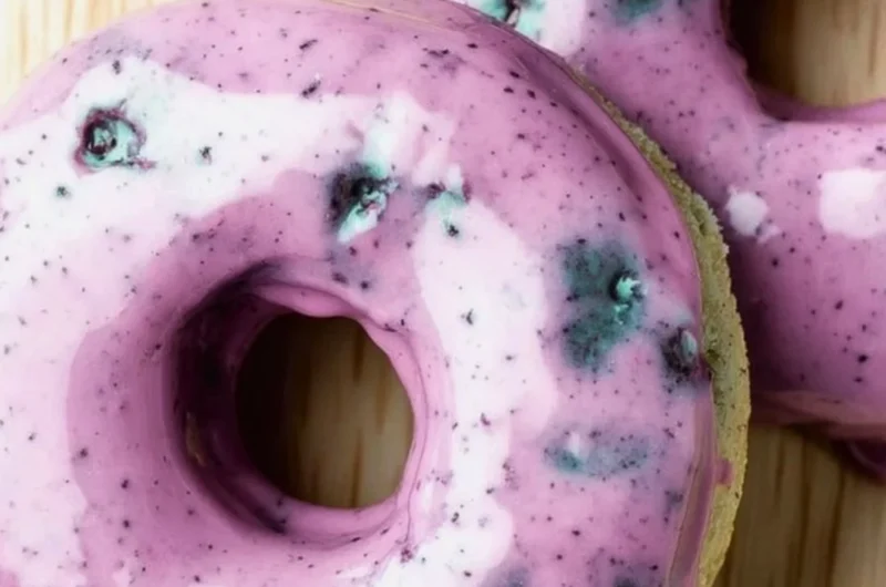 Freshly baked blueberry cake donuts topped with a glaze and blueberries.