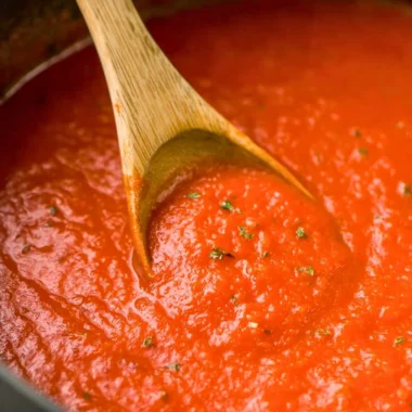 Homemade marinara sauce in a pot with fresh herbs and ingredients.