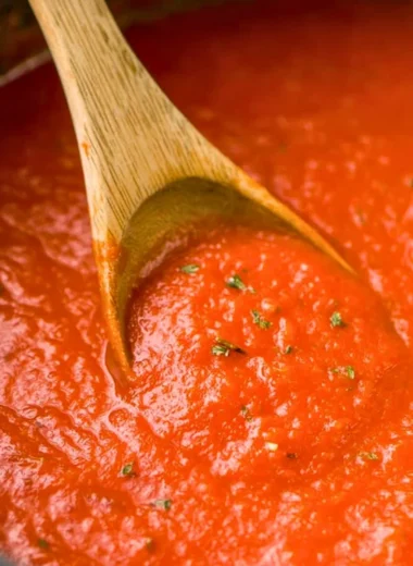Homemade marinara sauce in a pot with fresh herbs and ingredients.