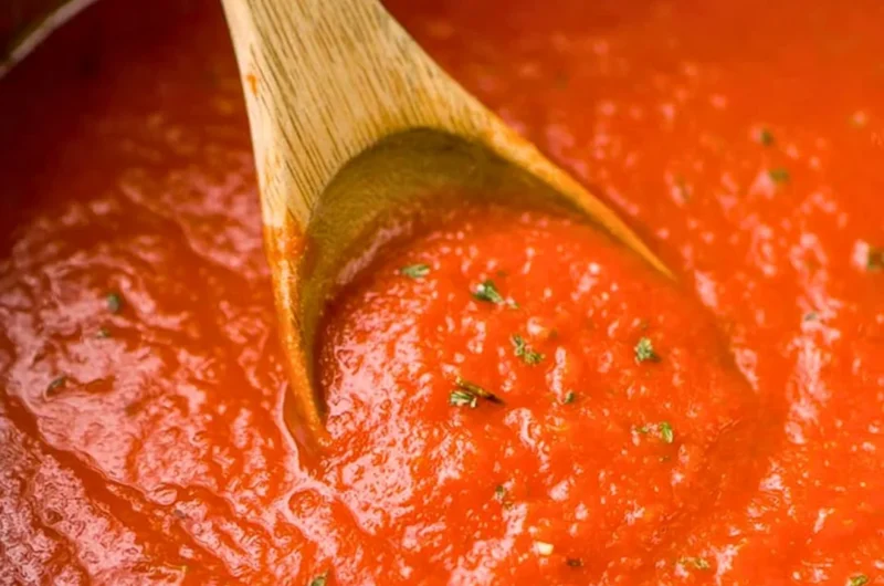 Homemade marinara sauce in a pot with fresh herbs and ingredients.