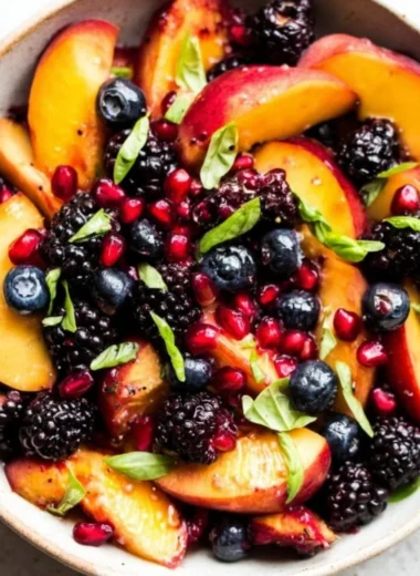 A vibrant bowl of Honey Lime Basil Peach Fruit Salad garnished with fresh basil.