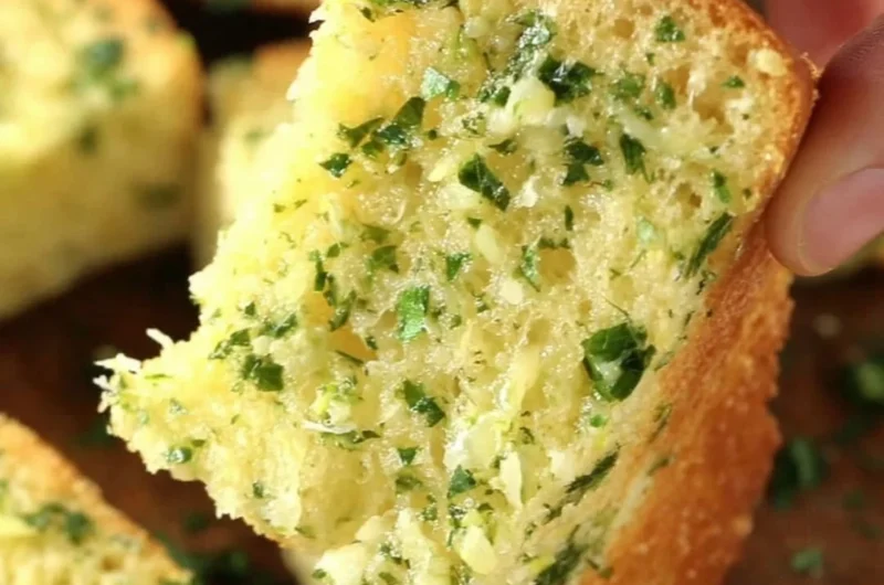 Homemade garlic bread with butter and herbs on a wooden table