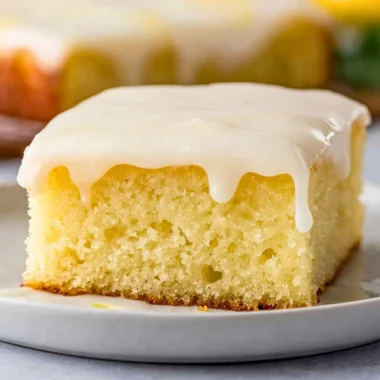 Delicious lemonade poke cake topped with lemon frosting and fresh lemons.