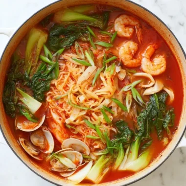 A bowl of spicy seafood noodle soup garnished with herbs and chili