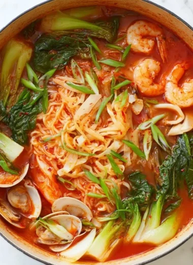 A bowl of spicy seafood noodle soup garnished with herbs and chili