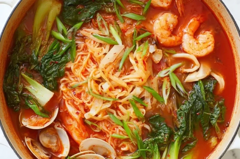 A bowl of spicy seafood noodle soup garnished with herbs and chili